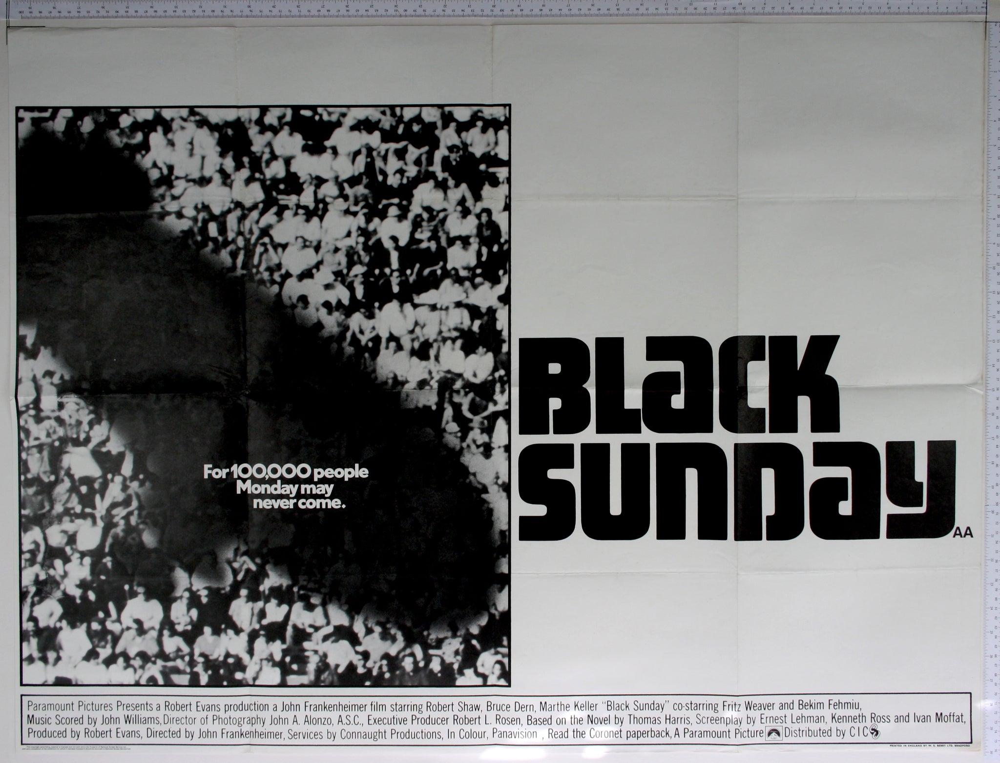 boxed black and white artwork of blimp shadow over sports crowd with large title in black to right, and bottom credit box