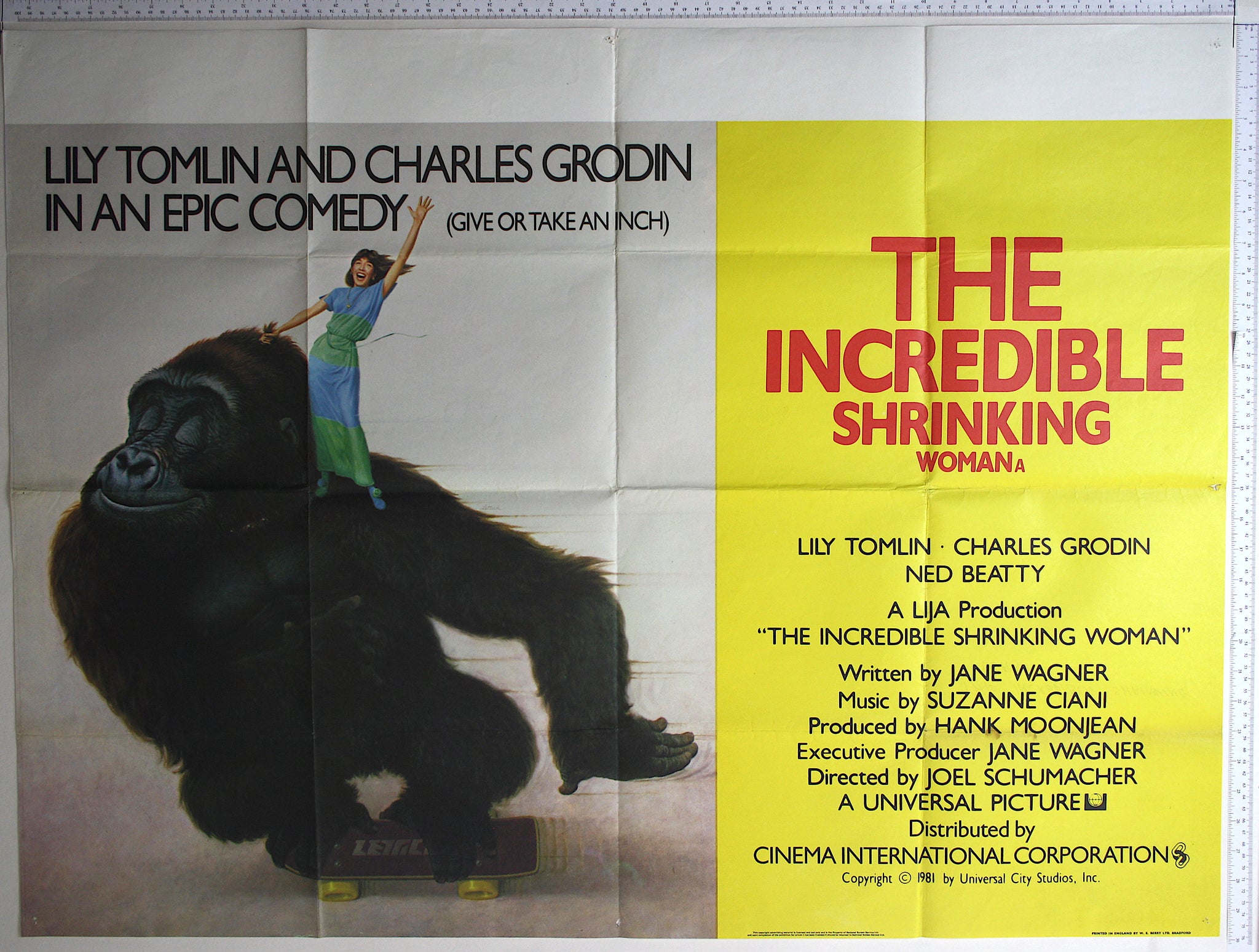 Tiny Tomlin standing on shoulder of gorilla, hanging onto a tuft of hair as it skateboards. 