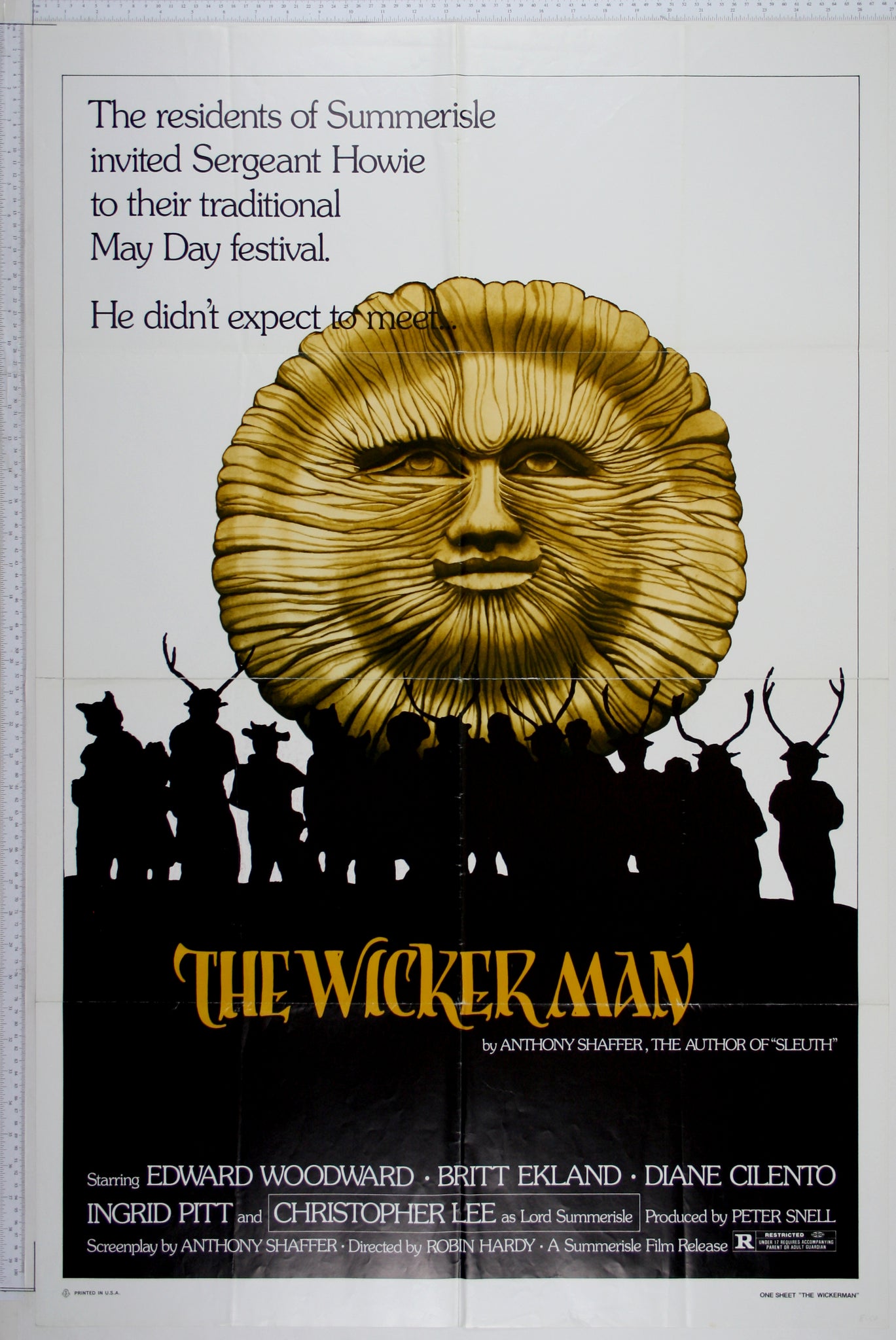 Wooden sun head looms over silhouettes of townspeople dressed in pagan, antlered costumes.